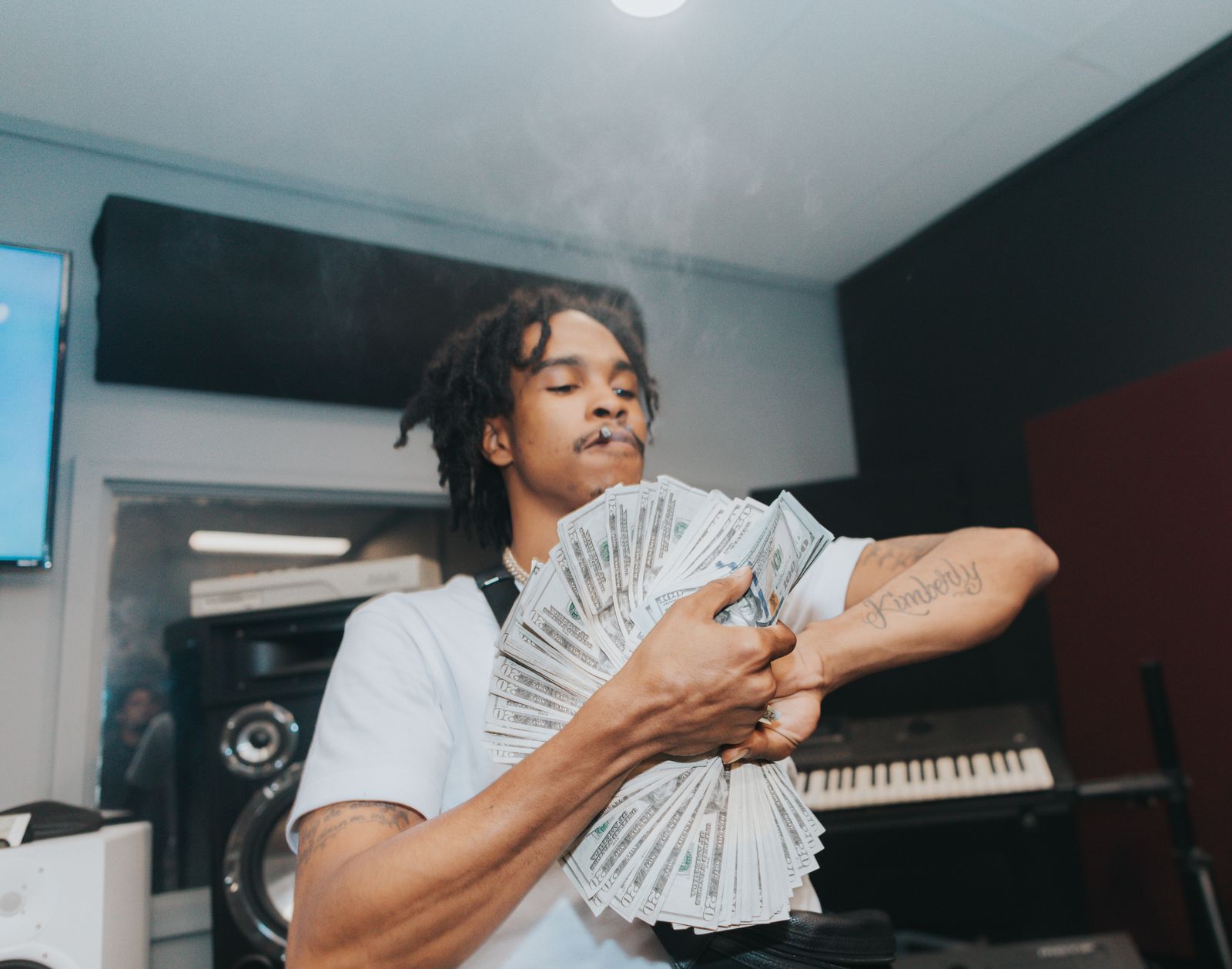 Un jeune homme brandissant de l'argent dans un studio de musique moderne, dégageant richesse et style.